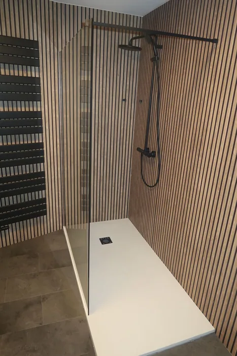 Inloopdouche met witte douchebak, glazen wand en zwarte regendouche tegen houten lamellenpanelen