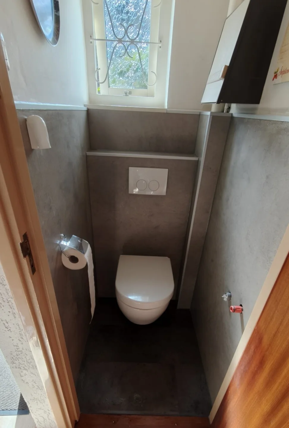 Toilet: situatie na het werk — Staand toilet met fonteintje en witte tegels wordt een hangtoilet met voorzetwand en betonlook wandpanelen.